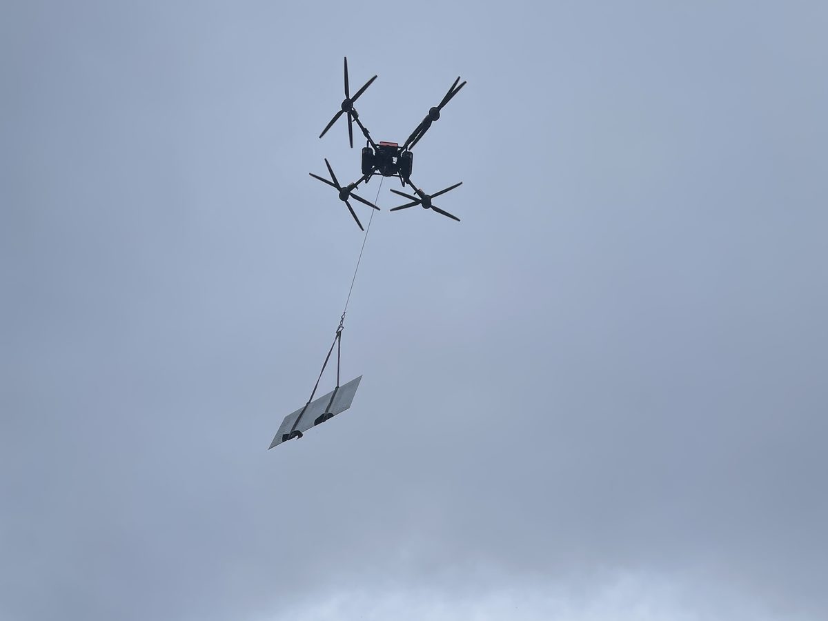 雨天の中、縞鋼板を吊り下げて運ぶ DJI FlyCart 100